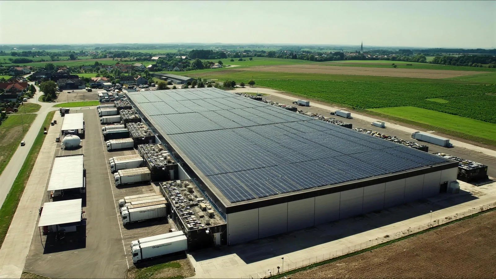 Luftaufnahme eines Logistikzentrums mit Solardach, Lkw an den Laderampen und Feldern im Hintergrund